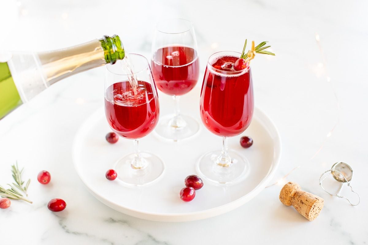 A white tray with 3 glasses full of poinsettia cocktail, champagne being poured in