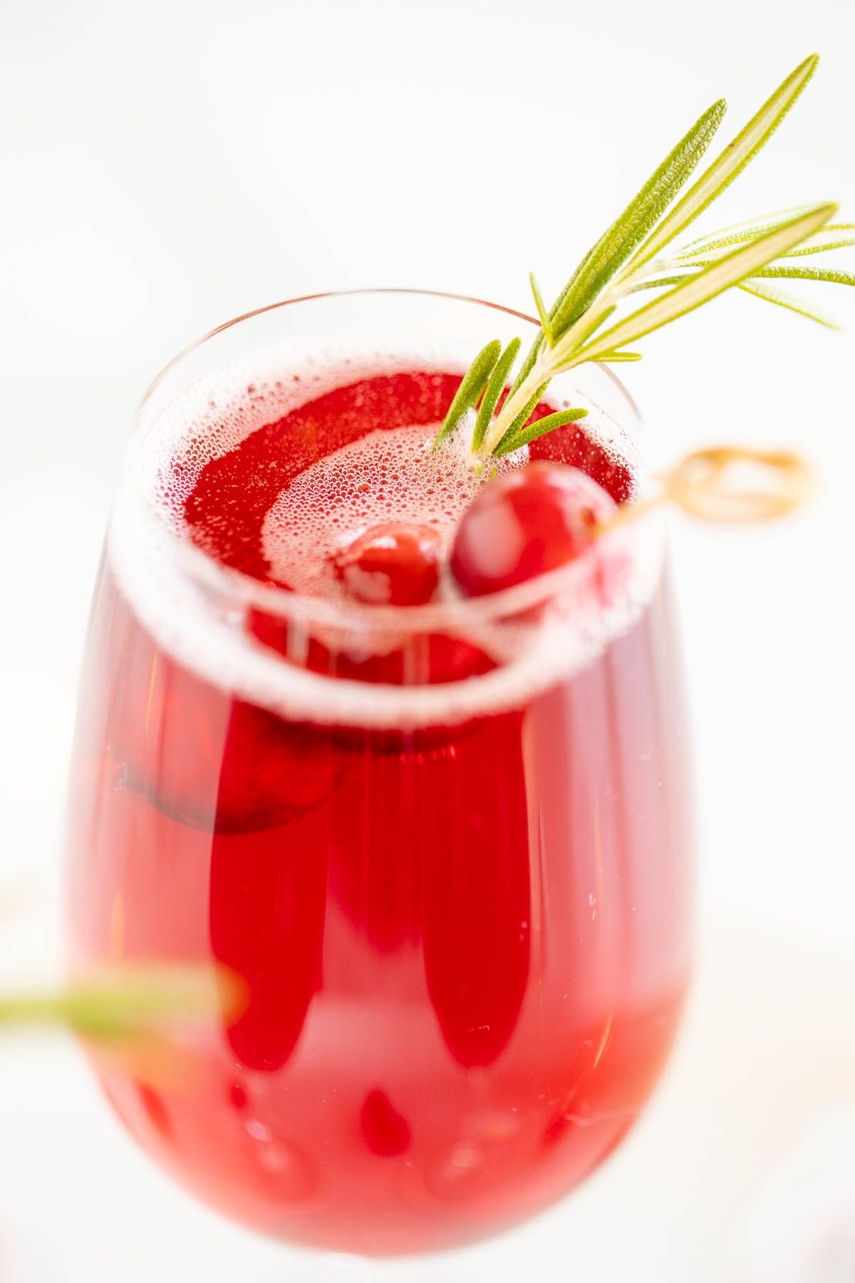 A glass full of a champagne poinsettia cocktail for Christmas, cranberry and rosemary garnish!