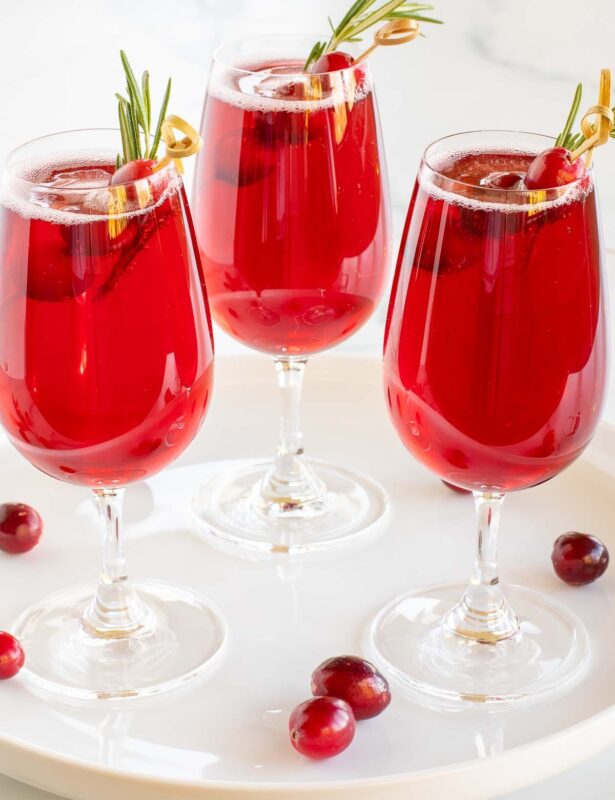 Poinsettia drinks on a white tray, cranberries and rosemary for garnish