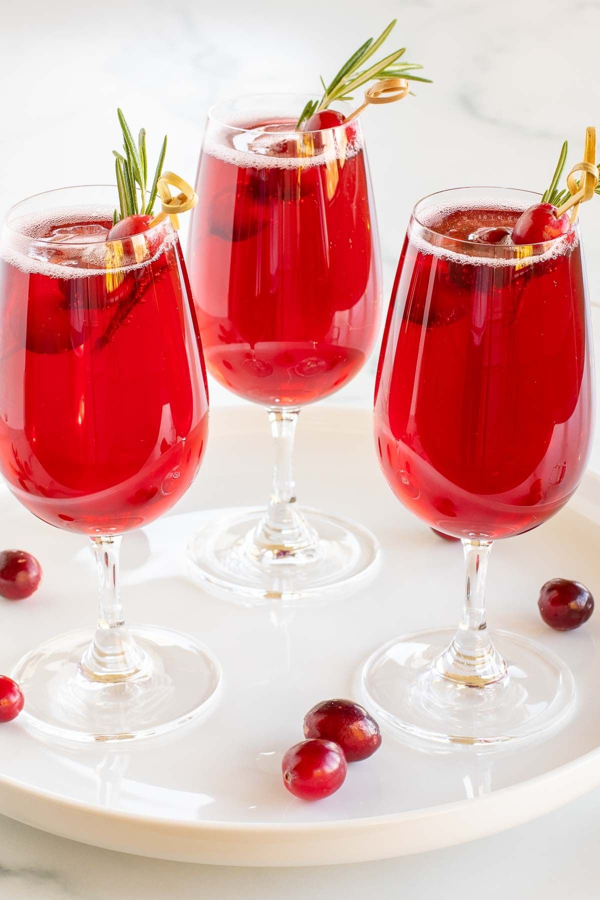 Poinsettia drinks on a white tray, cranberries and rosemary for garnish