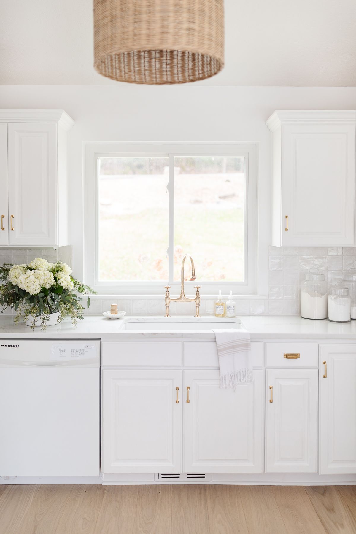 A white kitchen with a white tile backsplash and flowers by the sink