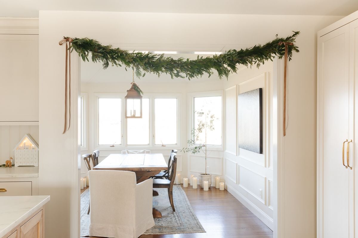 Fresh greenery garland draped over a doorway between a kitchen and dining space
