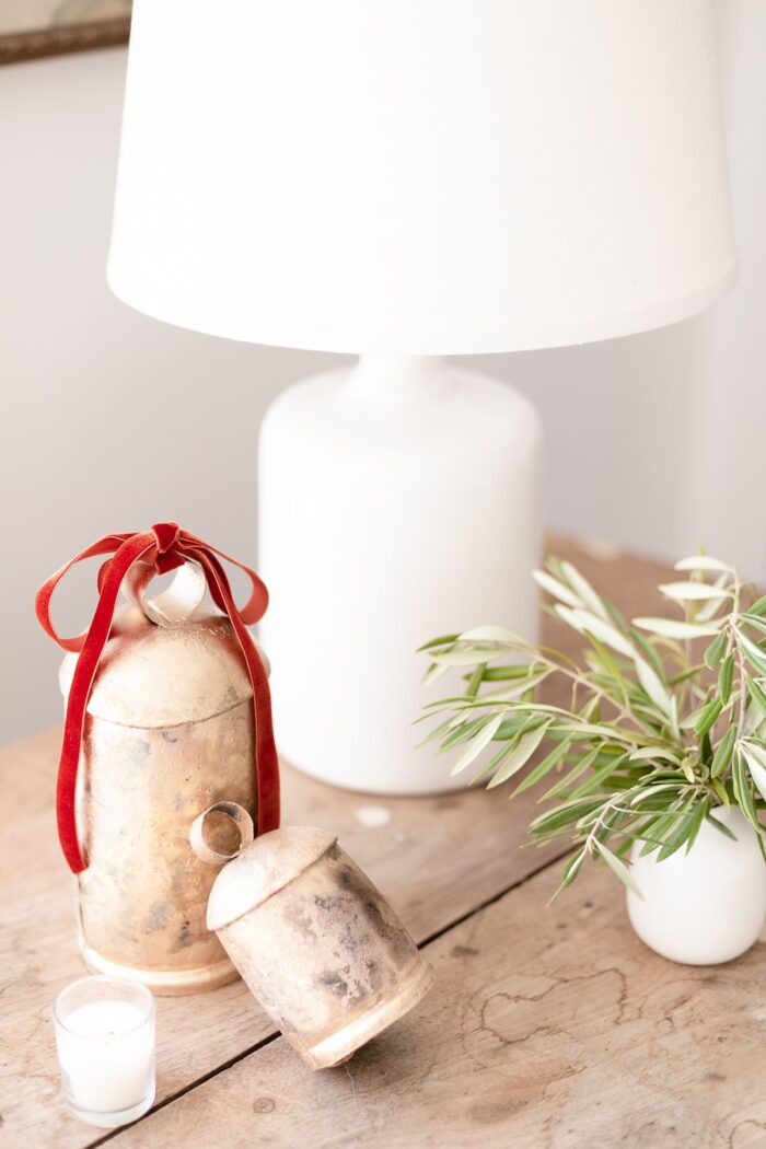 Brass bells and a white lamp on a rustic wood table