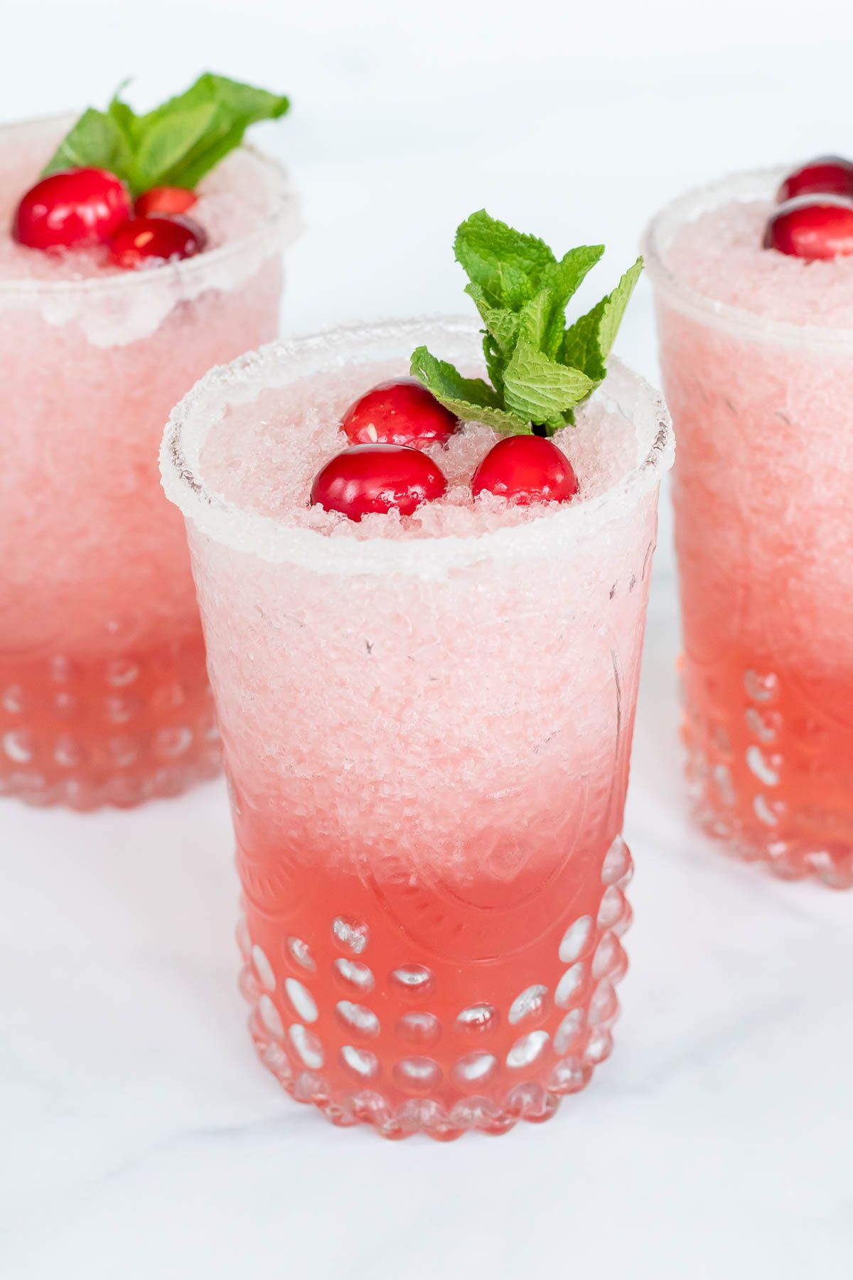 Pretty clear glasses full of Mistletoe Margaritas, topped with fresh mint and cranberries.