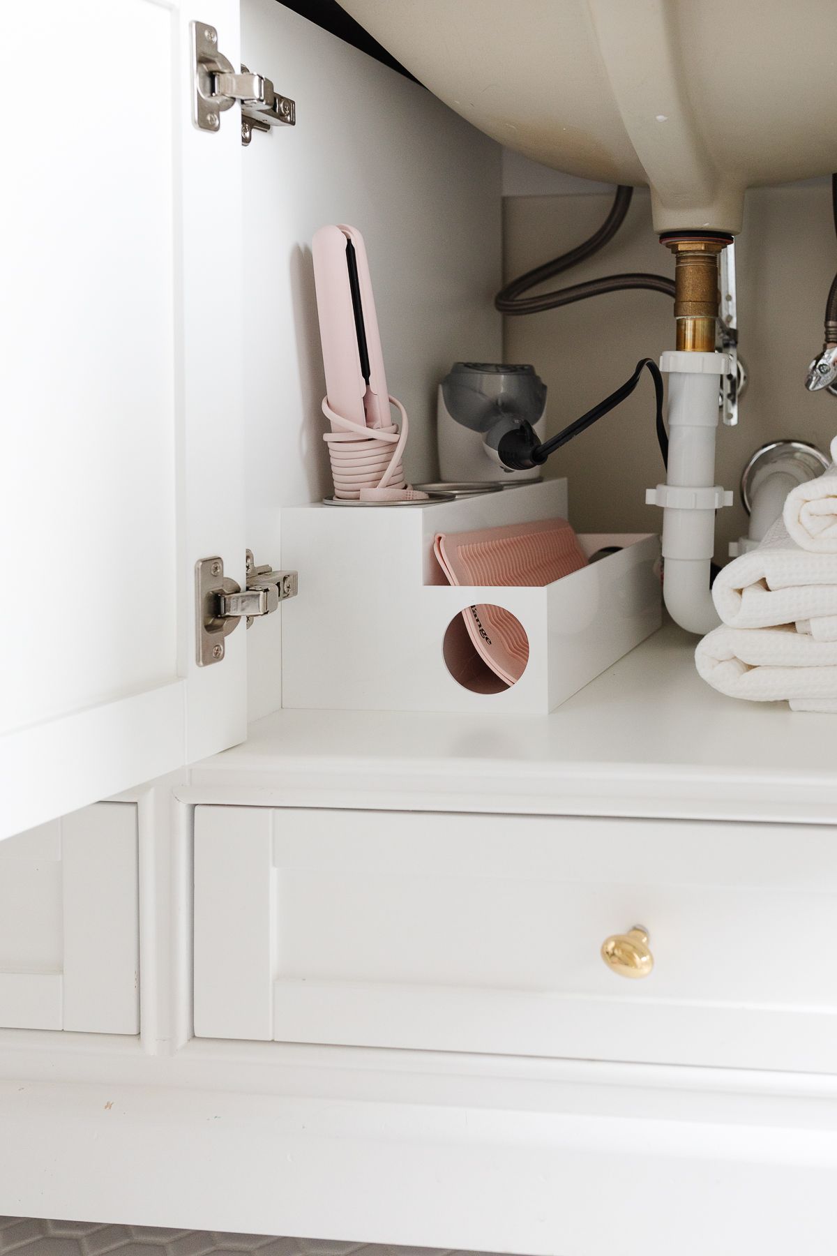 A white bathroom cabinet organization of under sink towels and hair supplies