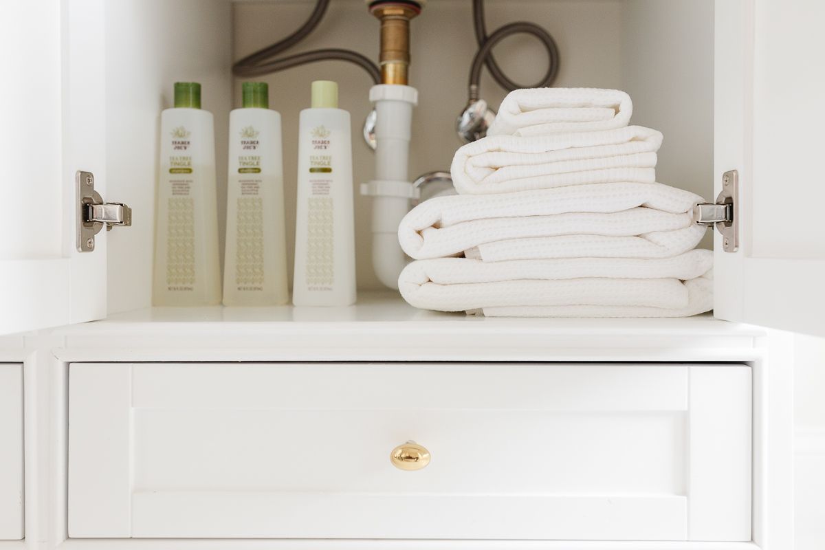 An under bathroom sink organization with shampoo and white towels.