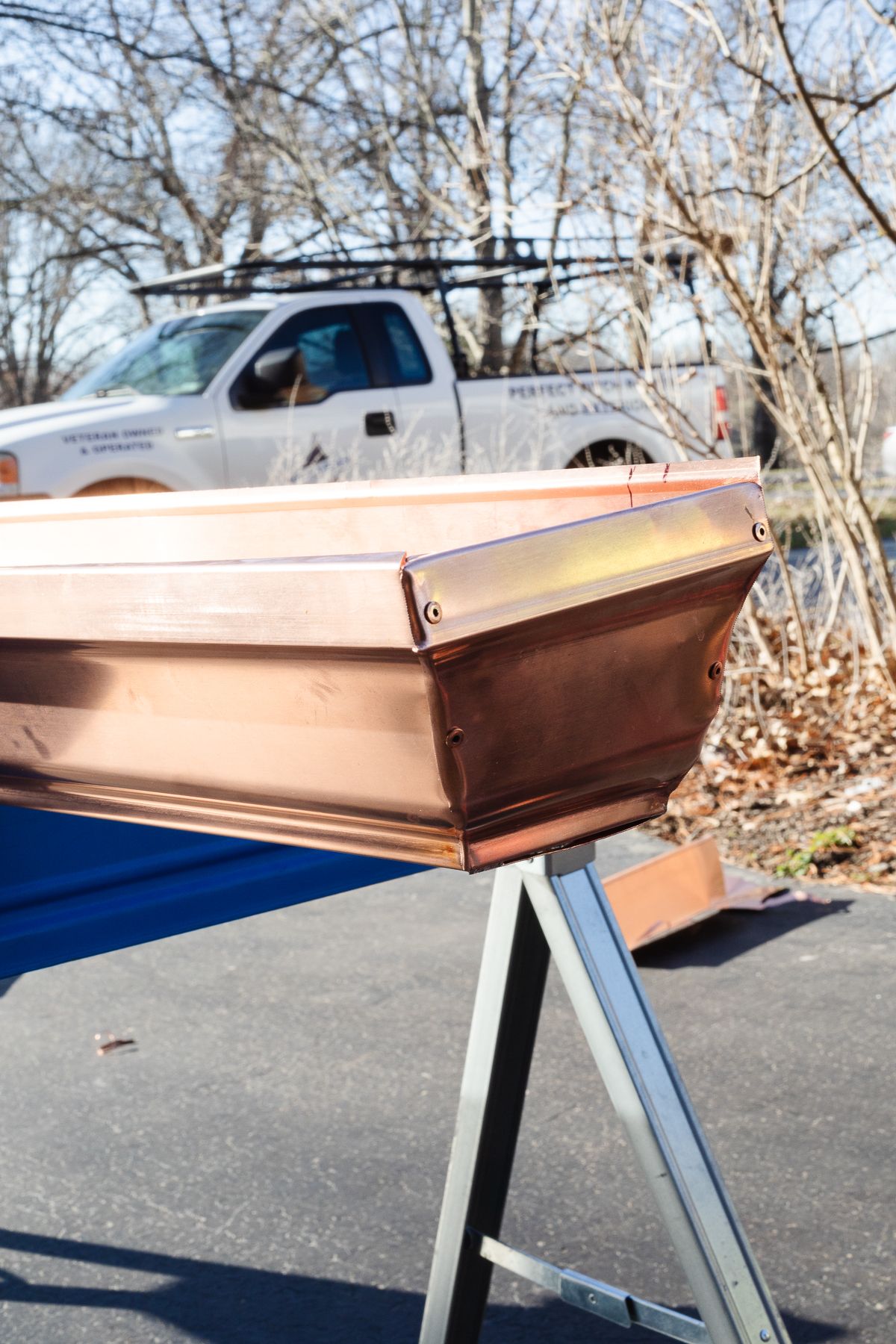 A copper gutter on a workbench with a work truck in the background
