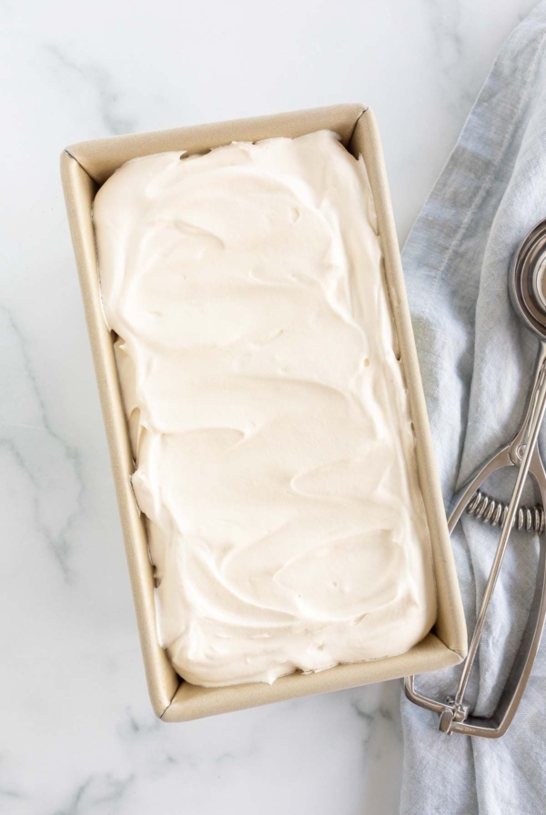 A gold loaf pan filled with homemade mascarpone ice cream, scoop to the side