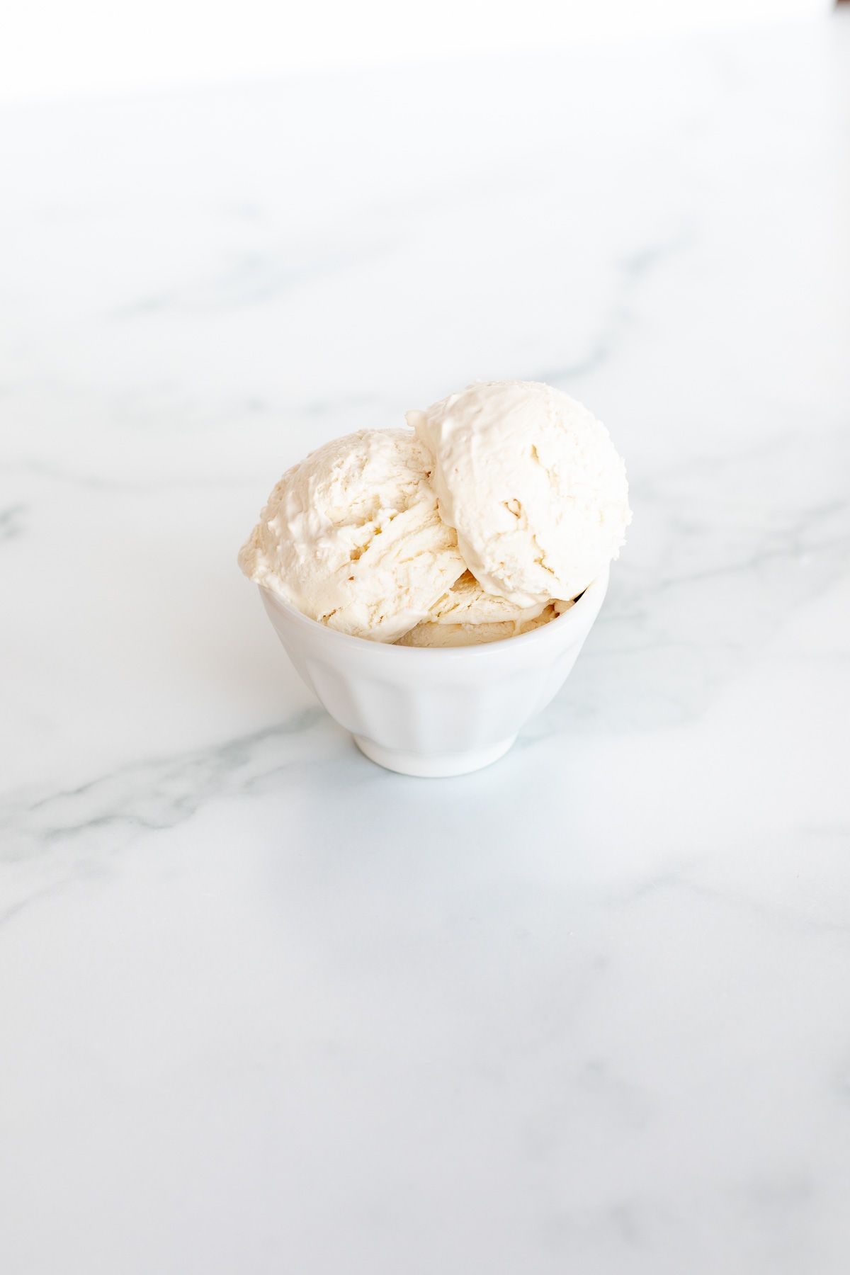 A white bowl on a marble surface, filled with frozen mascarpone ice cream