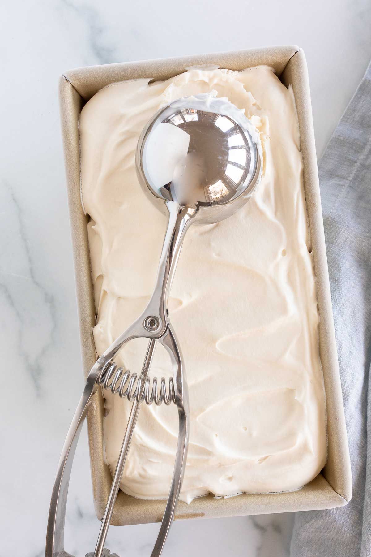 A gold loaf pan filled with homemade mascarpone ice cream, ice cream scoop on top