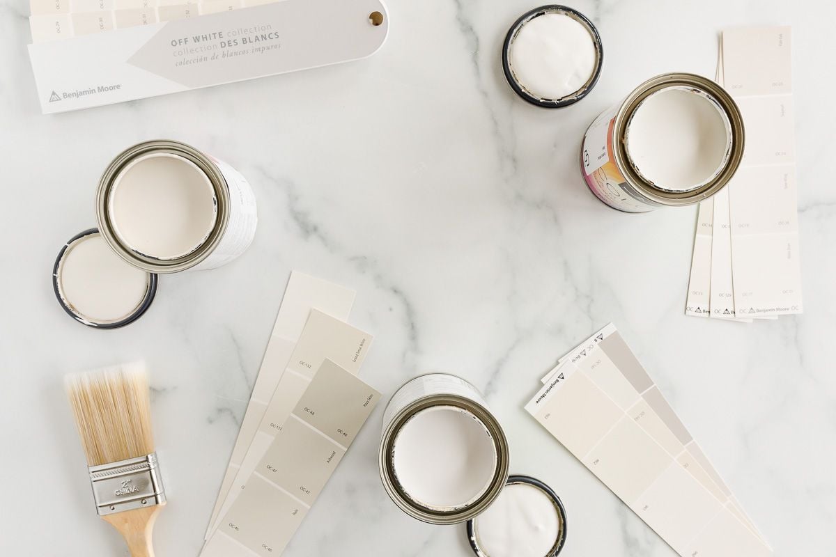 Open cans of warm whites and paint swatch cards laid out on a marble surface.