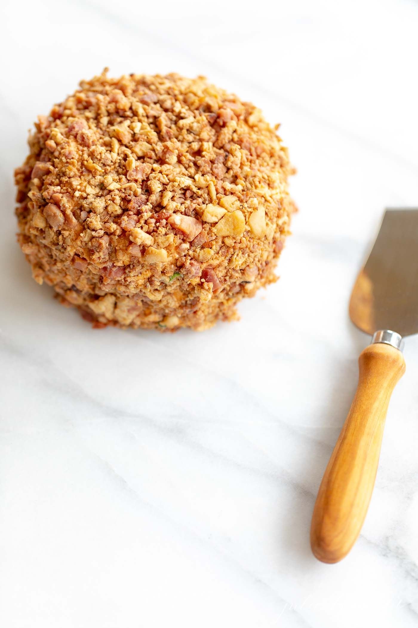 Marble surface, bacon ranch cheese ball with a spreader knife to the side.