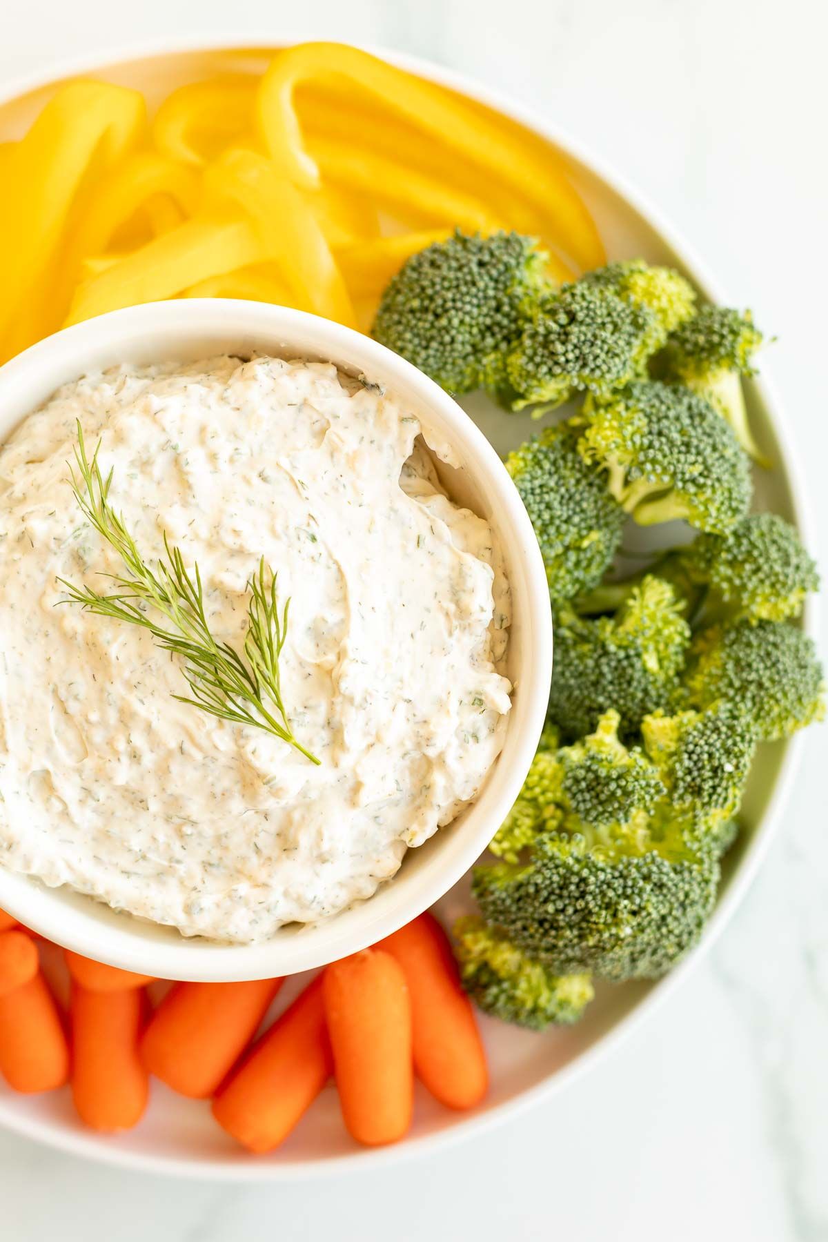 A round platter full of veggies and dill dip. 