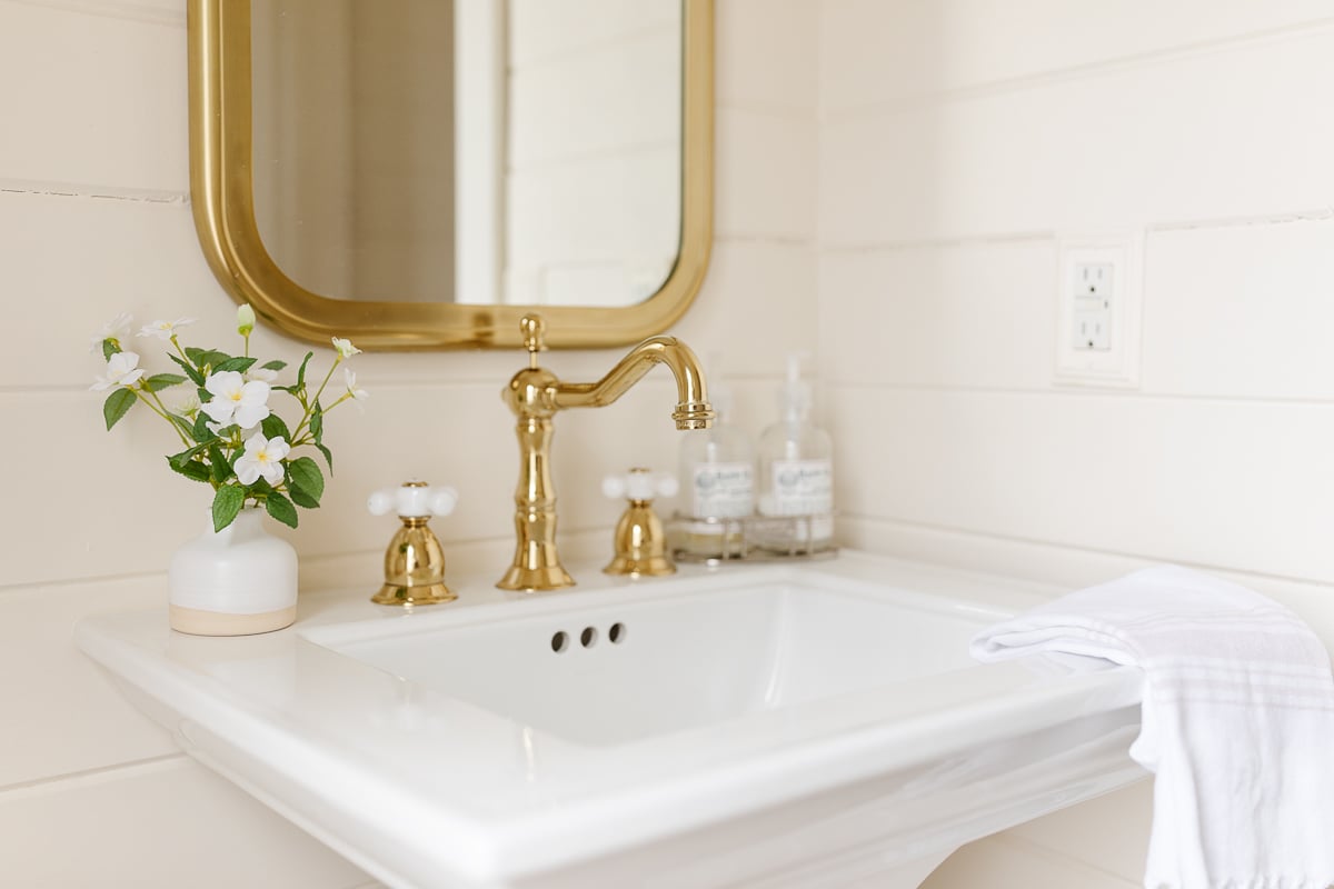 a white bathroom with a brass sink and mirror.