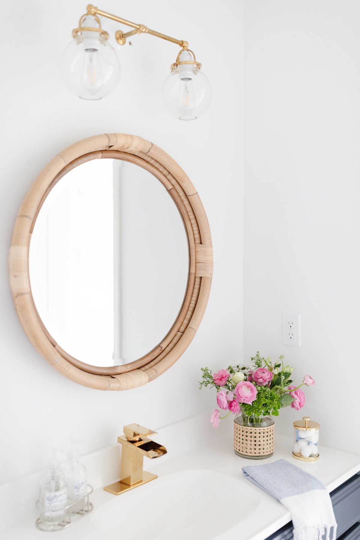 a bathroom with a round mirror, brass bathroom faucets and flowers.