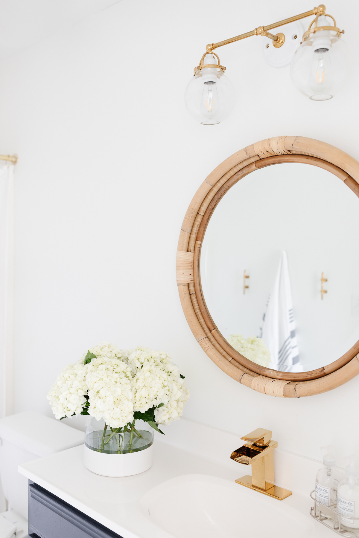 a bathroom with a round mirror and brass bathroom faucets.