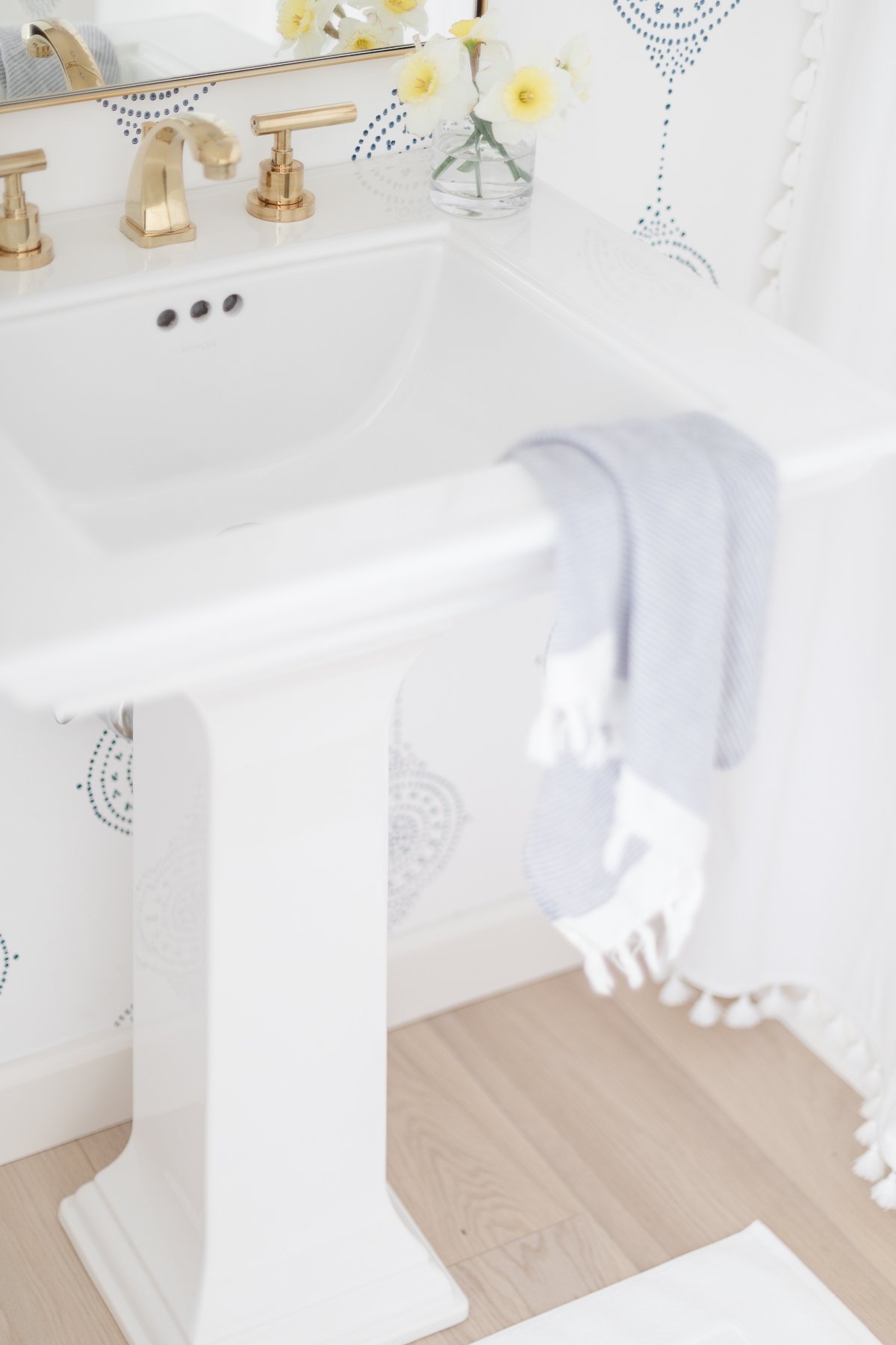 A bathroom with a white sink and blue wallpaper featuring brass bathroom faucets.