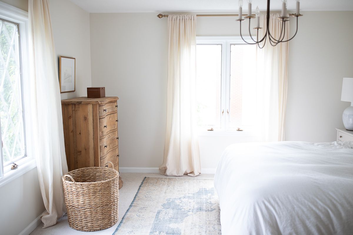 A primary bedroom with carpeted floor that have a vintage turkish rug placed on top, and a wood dresser in the corner.