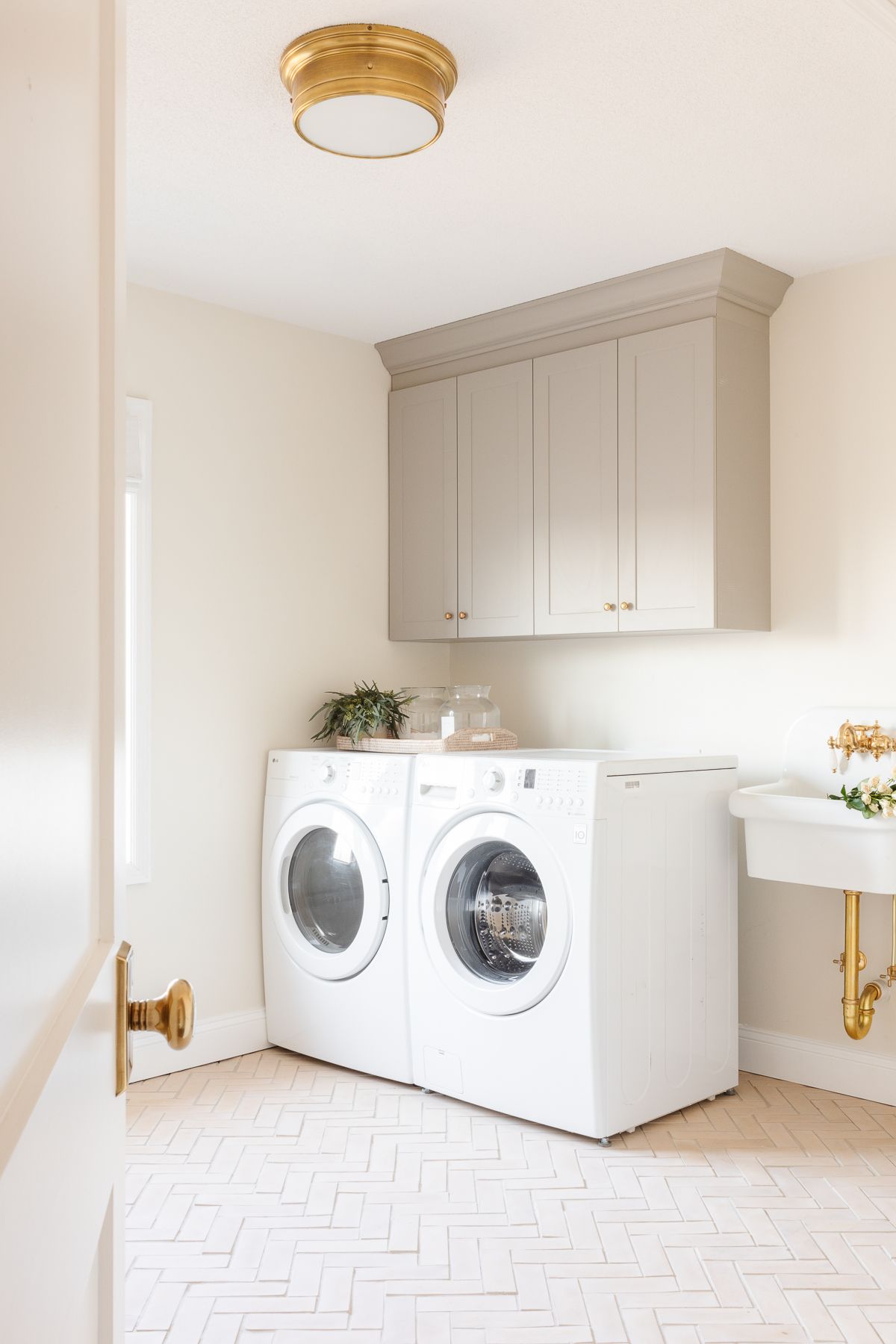 A laundry room with cream walls, greige cabinets and herringbone floors. 