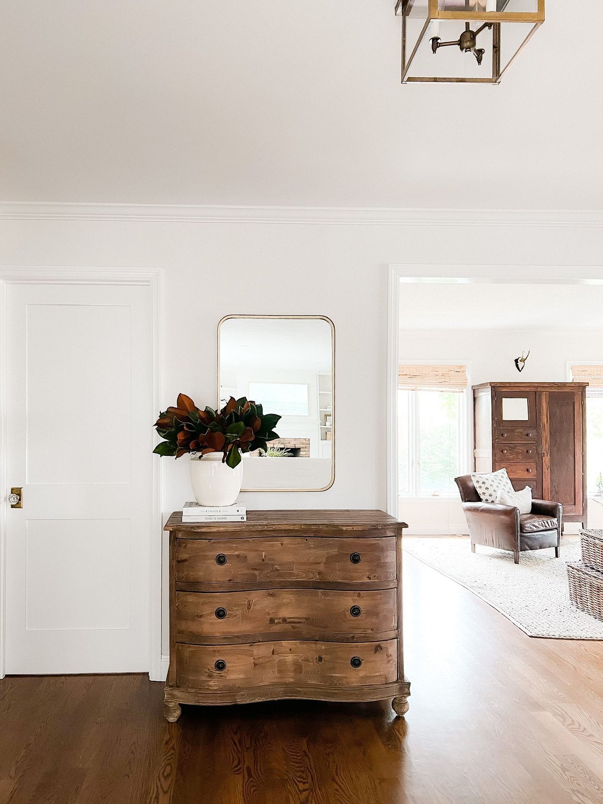 An entryway in a home with wood floors and a wood dresser with magnolia branches in a vase TeamJiX
