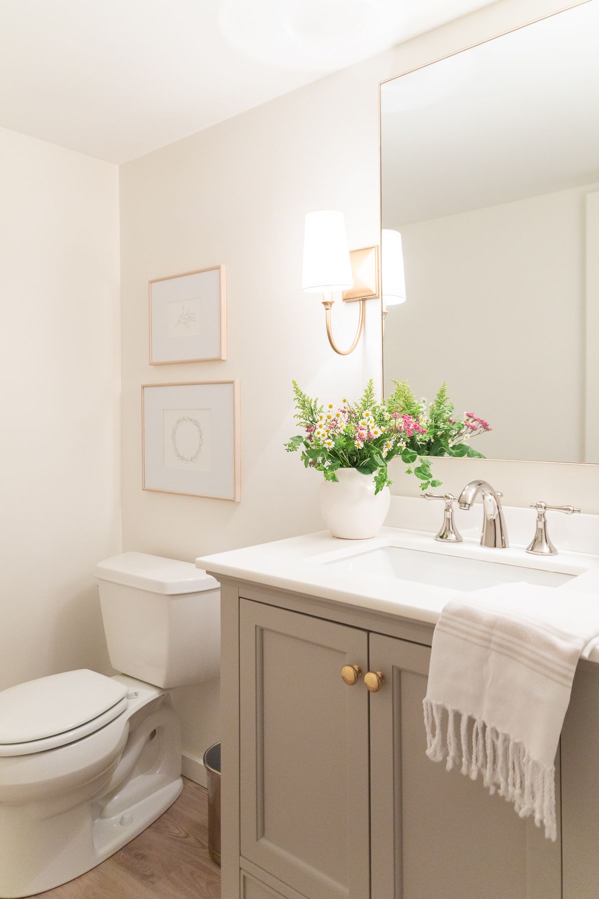 A bathroom with creamy walls and a greige vanity, with wall sconces for a cozy feel