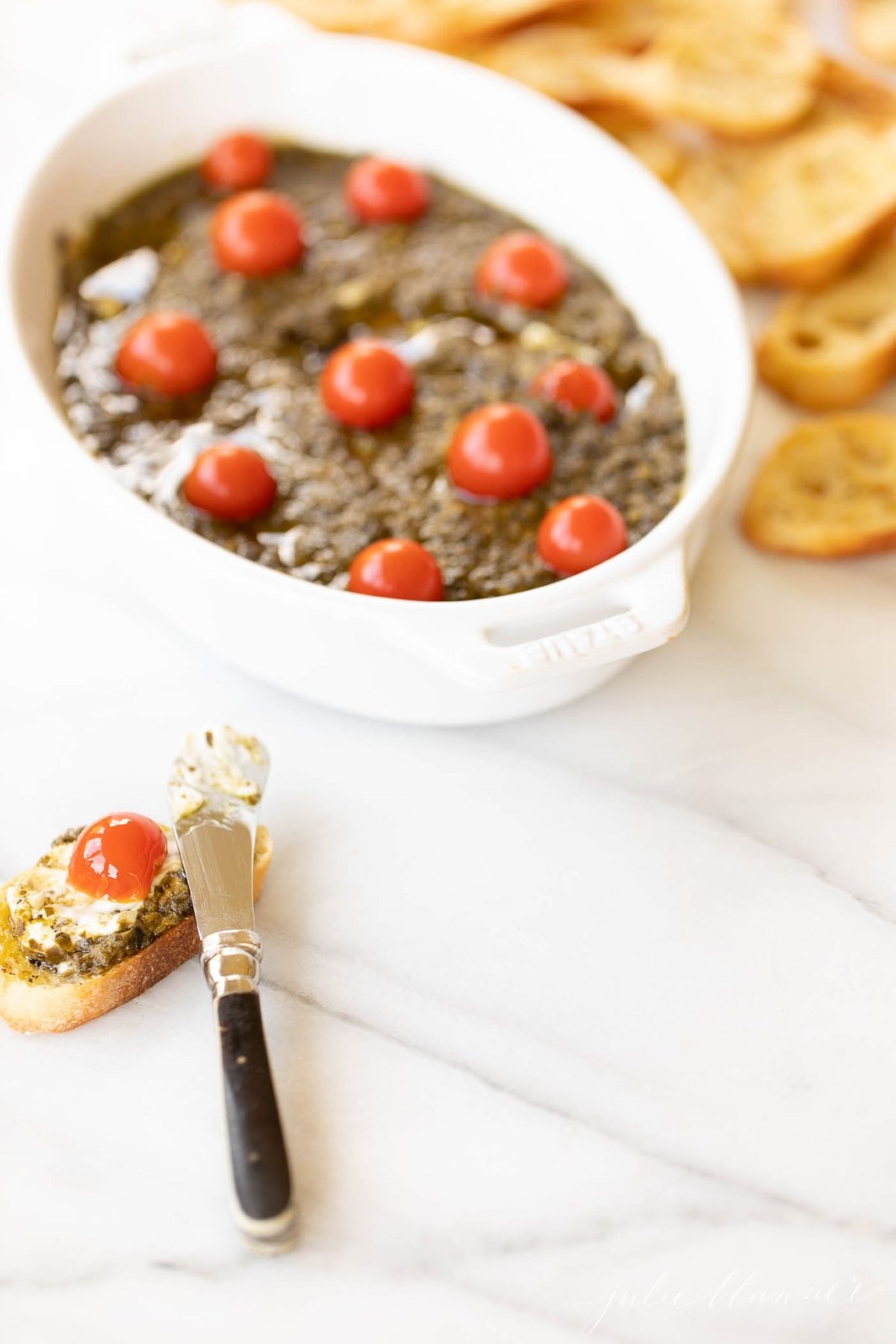 Homemade basil pesto in an oval dish with crostini slices to the side.