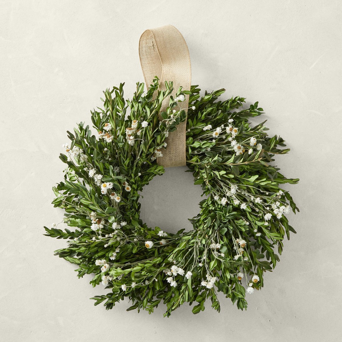 A spring wreath adorned with small white flowers and a burlap ribbon graces the light-colored wall.