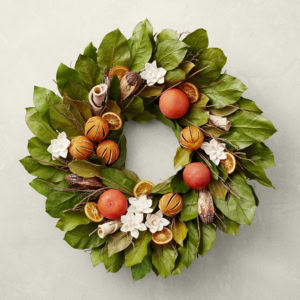 Spring wreaths featuring green leaves, oranges, peach-like fruits, white flowers, and cinnamon sticks are beautifully set against a light background.