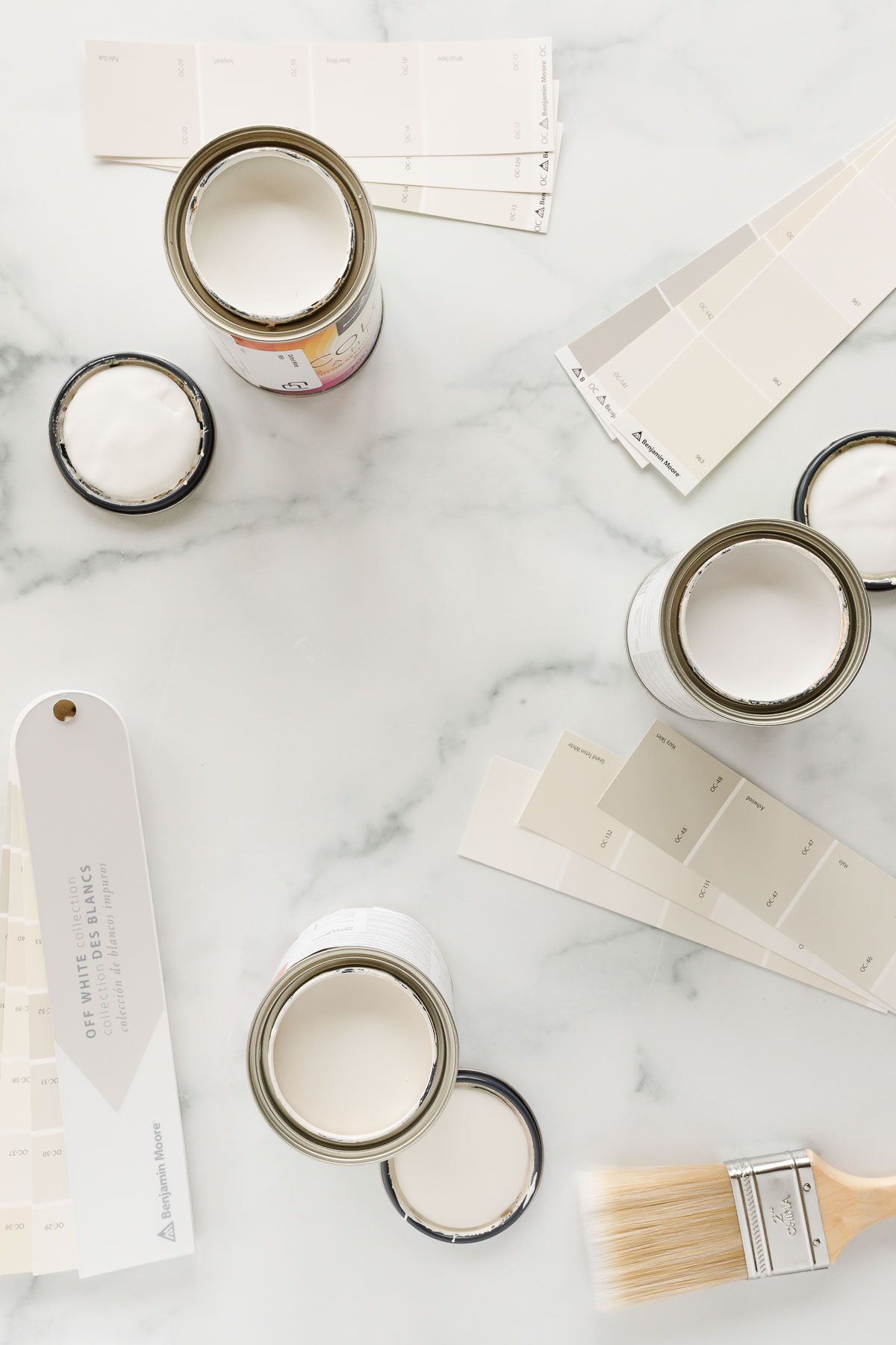 Paint samples and paint swatches in shades of cream on a marble countertop