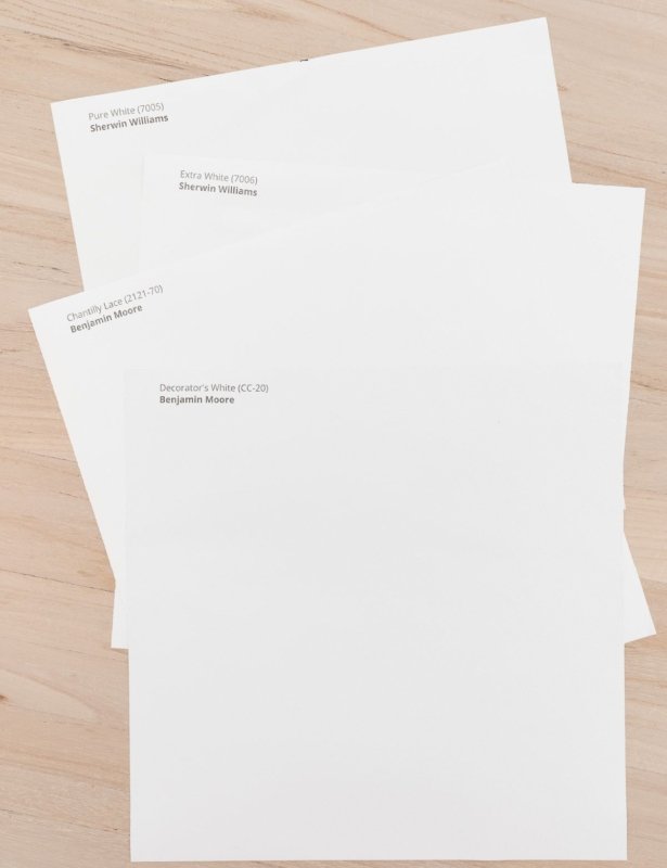 Shades of white Samplize paint samples laid out on a wood floor.