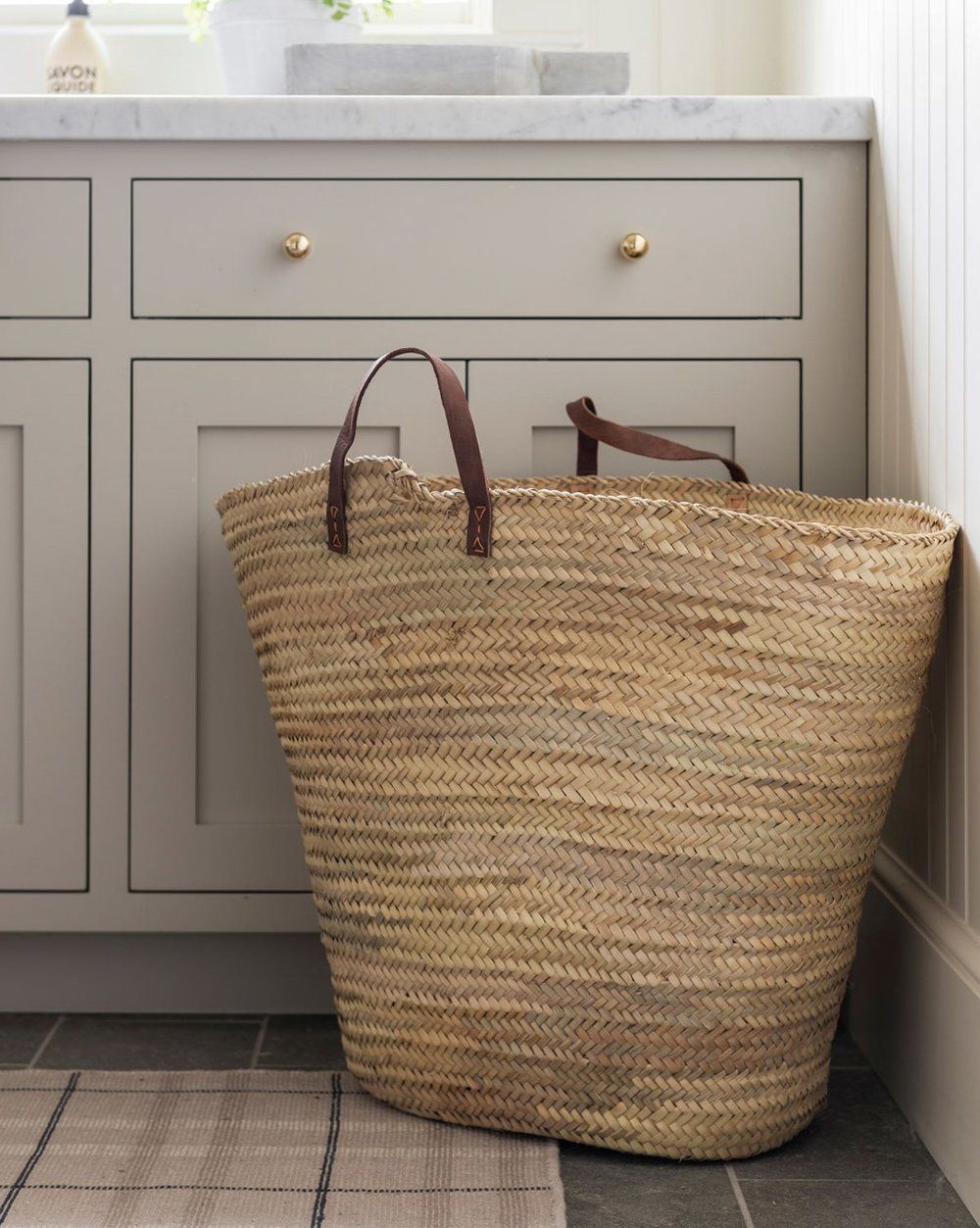 A laundry room cabinet painted in Revere Pewter with a straw tote bag in front.