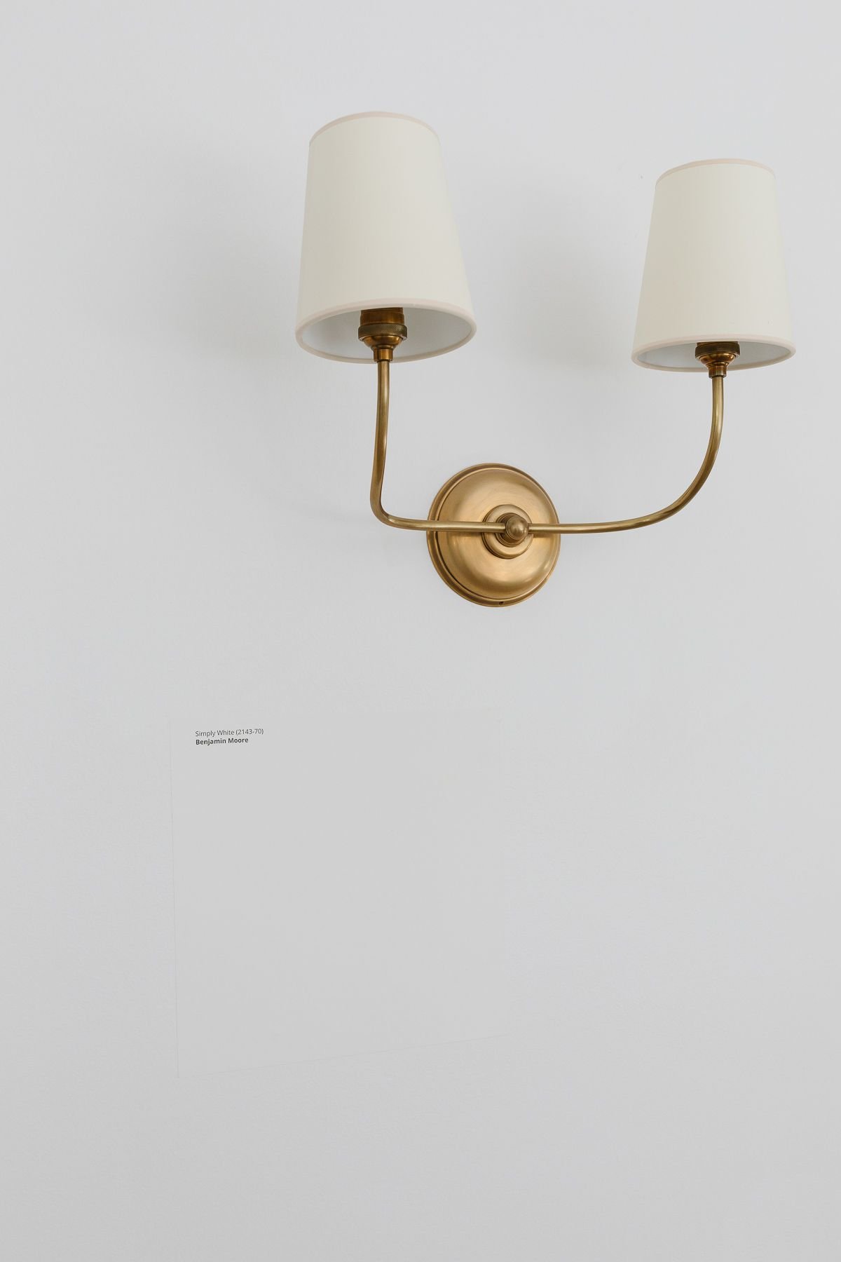 A Samplize paint sample on a white wall with a brass wall sconce above