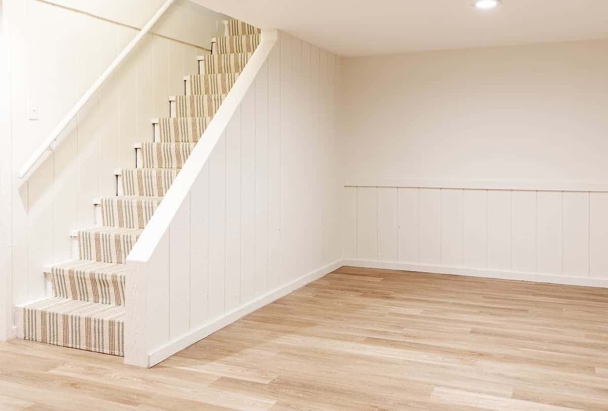 A diy stair runner in a blue and neutral stripe leading down to a white painted basement.