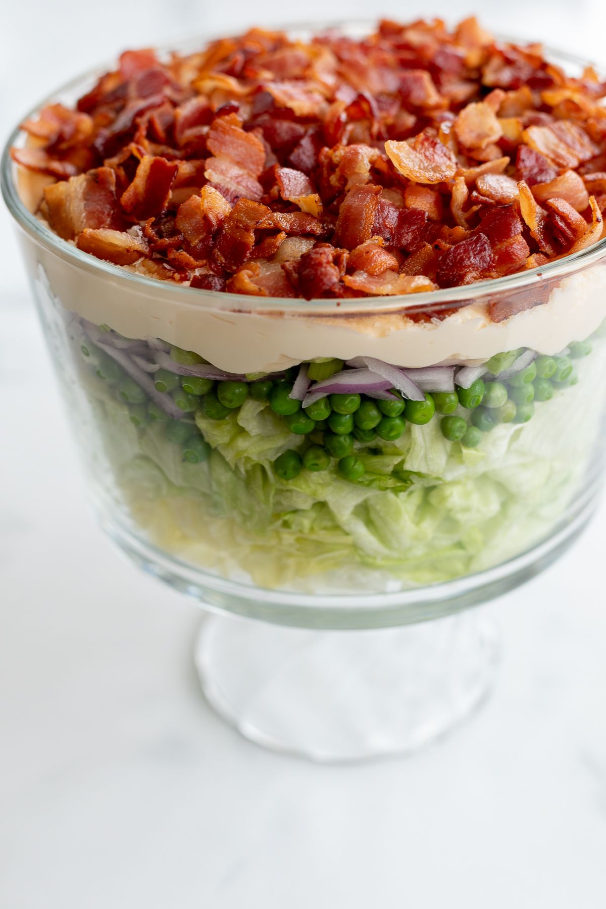 Seven layer salad topped with bacon on a marble countertop