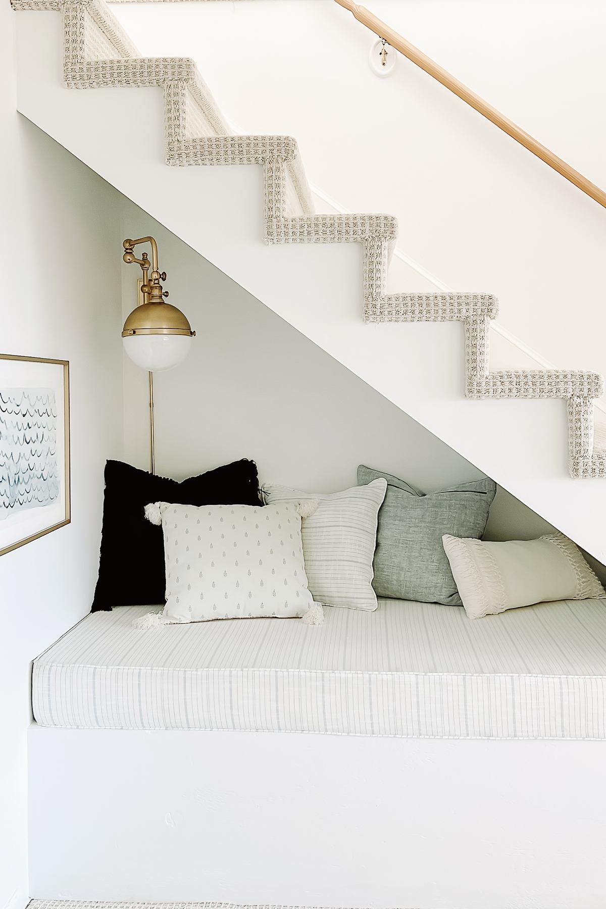 nook under an open staircase featuring a space for reading or sleeping, lots of blue and white pillows and a brass sconce