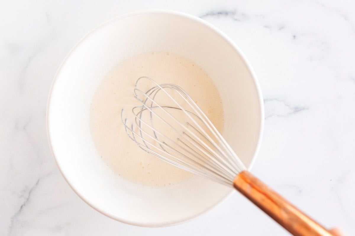 A sauce in a white bowl with a whisk to the side
