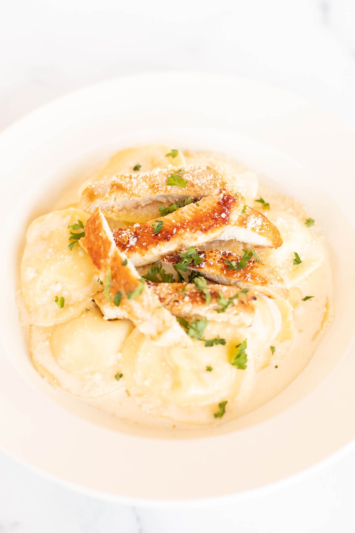 Tortelloni alfredo with grilled chicken on a white plate.