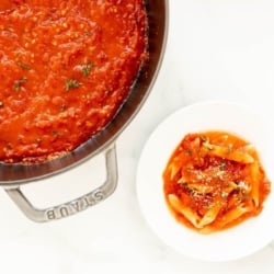 A cast iron pan full of arrabbiata sauce, plated sauce and pasta to the side