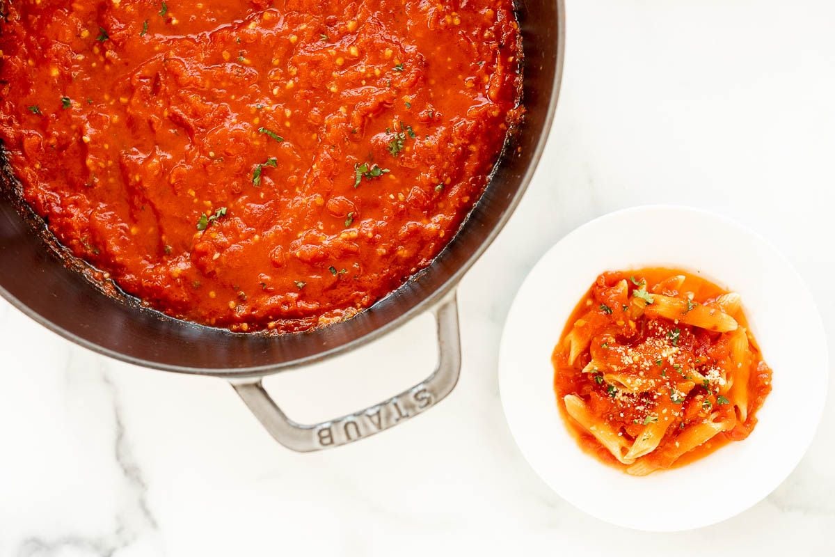 A cast iron pan full of arrabbiata sauce, plated sauce and pasta to the side