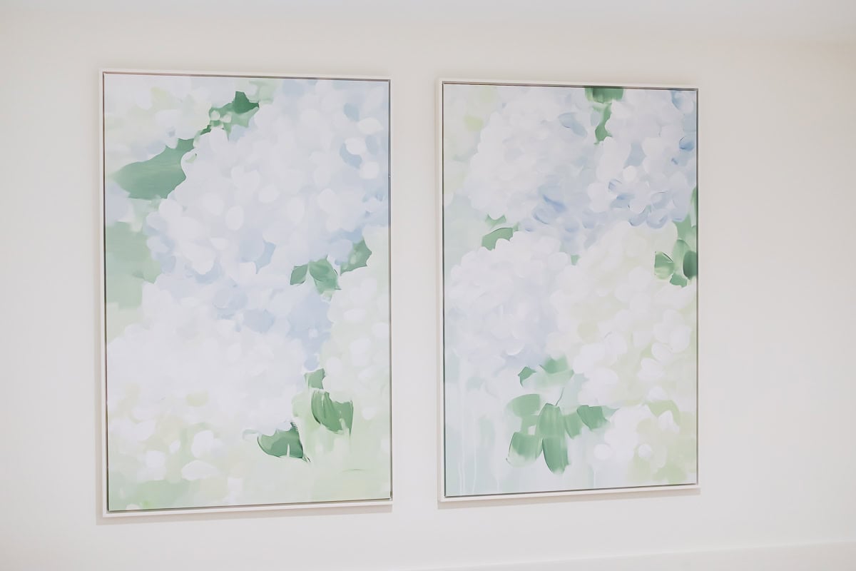 Two large framed paintings with abstract floral designs in soft pastel colors, mainly white, green, and blue, hang side by side on a plain white wall—an elegant amazon art find for any modern space.