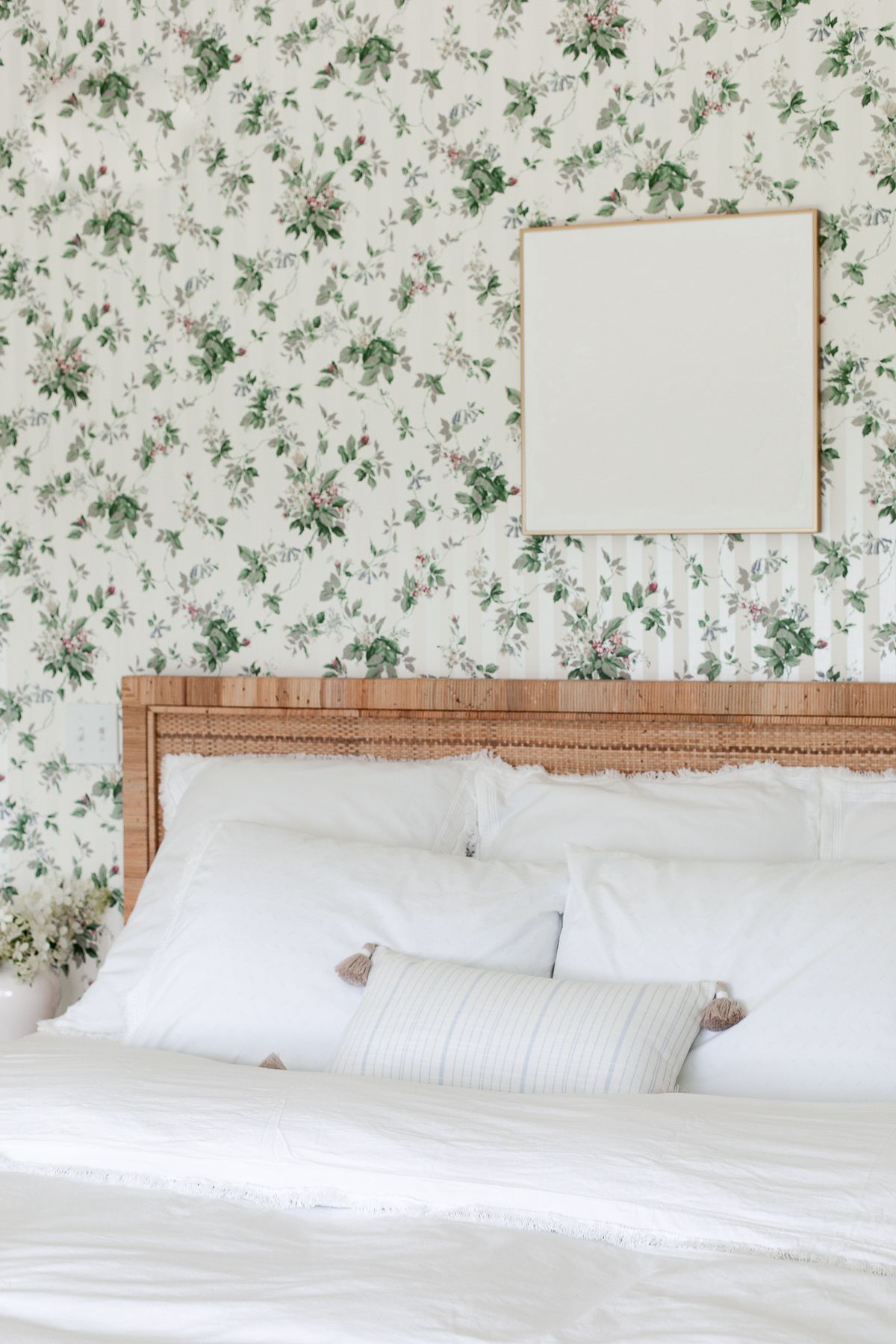 A wallpapered bedroom with white art over bed