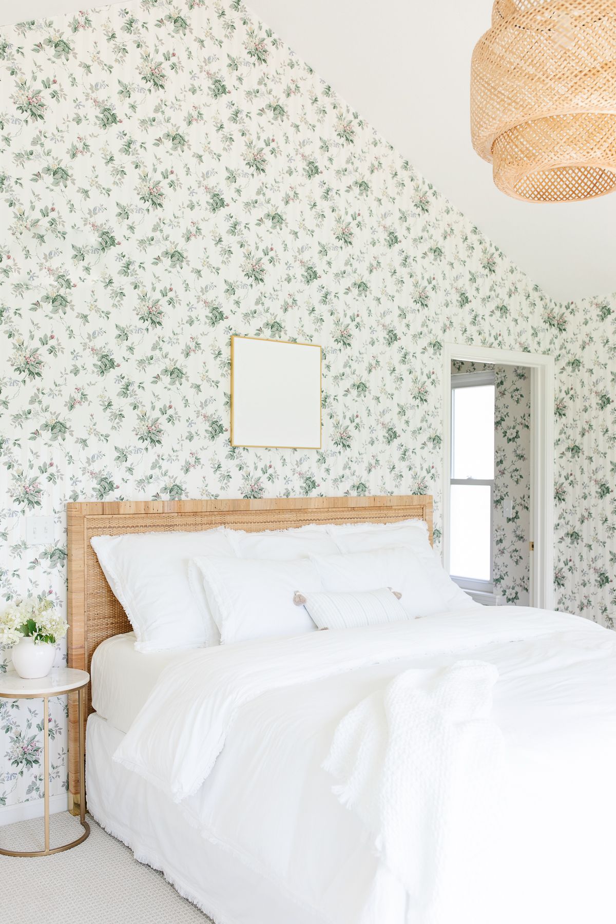 A wallpapered bedroom with white art over bed