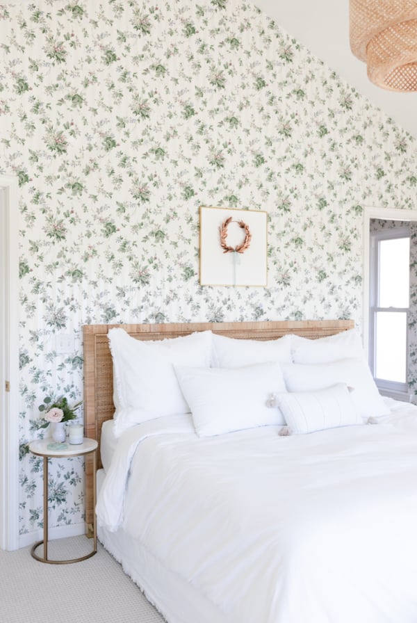 A white bedroom adorned with a stunning art piece above the bed, complemented by green floral wallpaper.