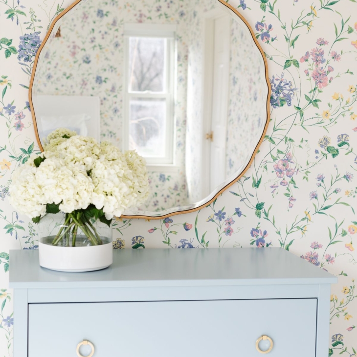 A bedroom with floral wallpaper and a dresser painted in a slate Blue color