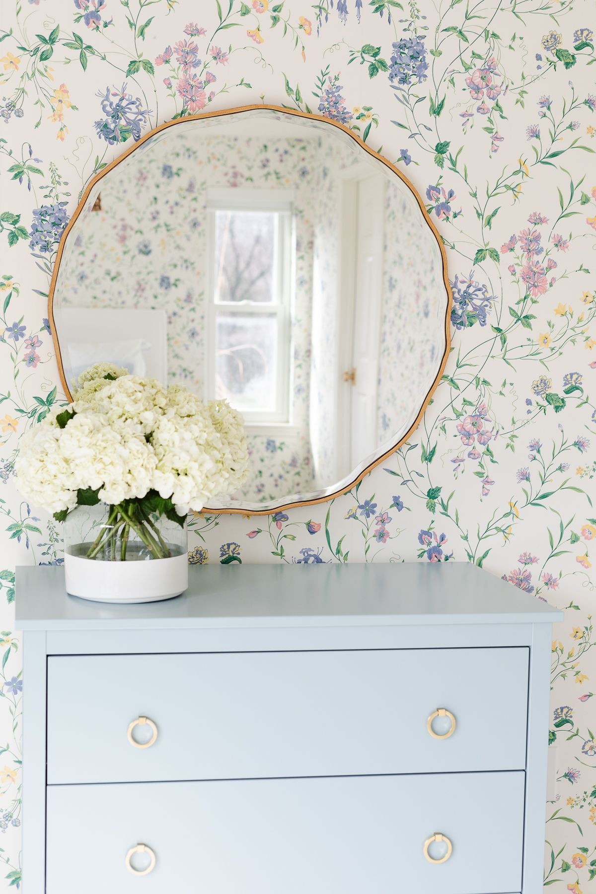 A bedroom with floral wallpaper and a dresser painted in a slate Blue color