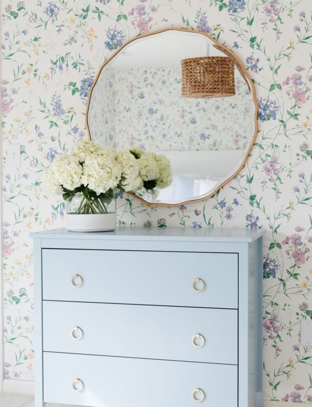 A bedroom with floral wallpaper and a dresser painted in a slate Blue color