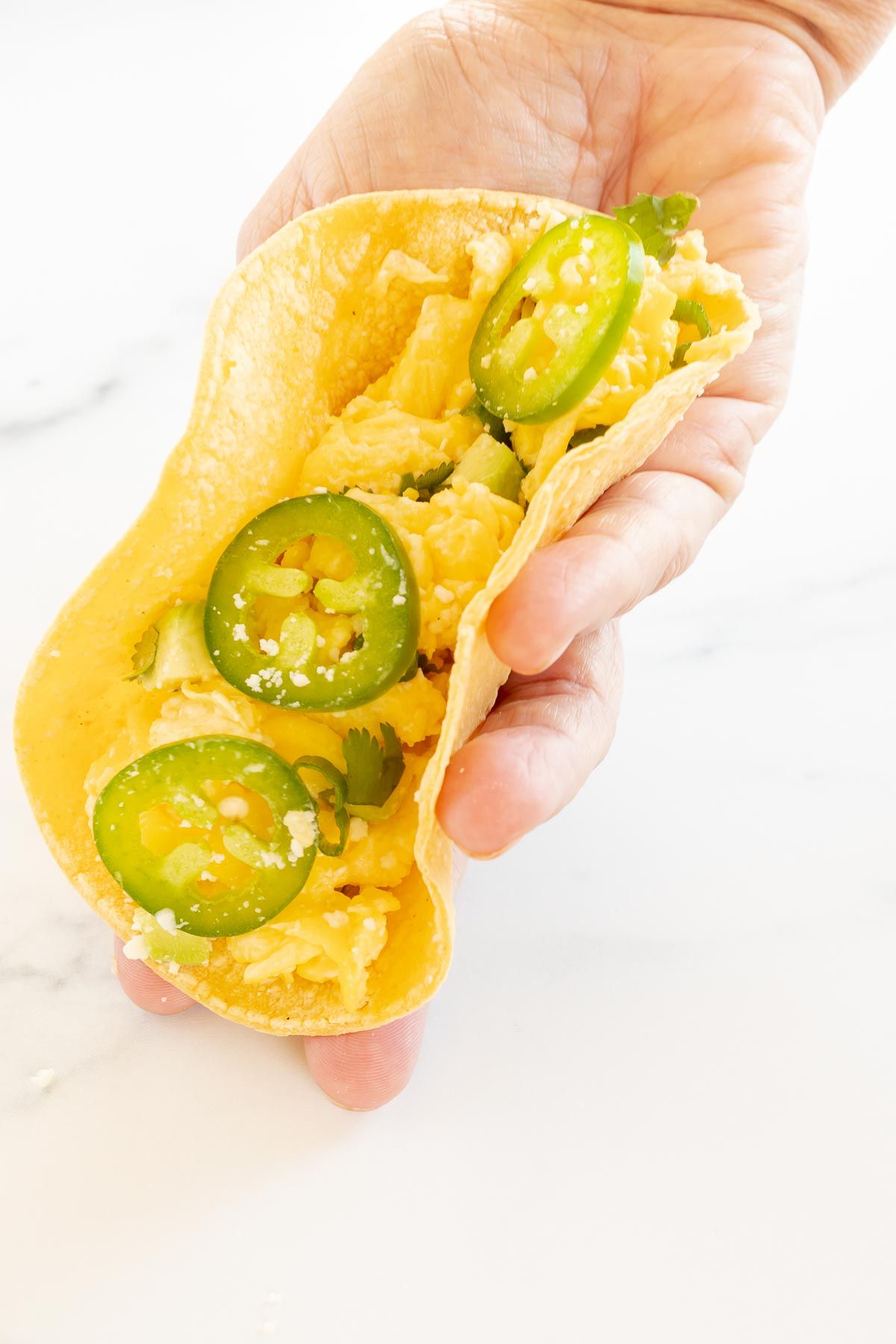 A hand holding a breakfast taco topped with sliced jalapenos