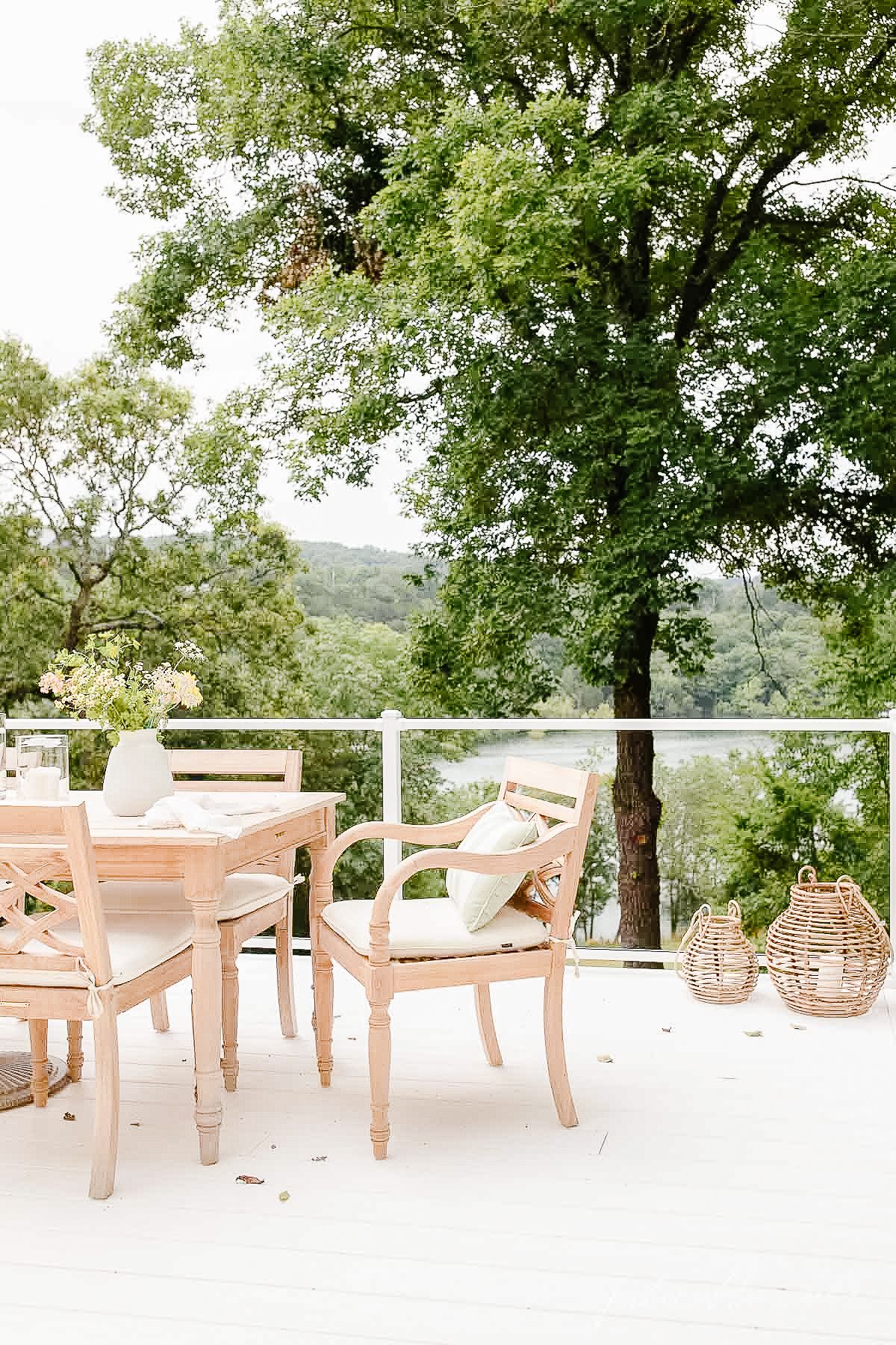 teak dining set on white deck with glass railing viewing lake 