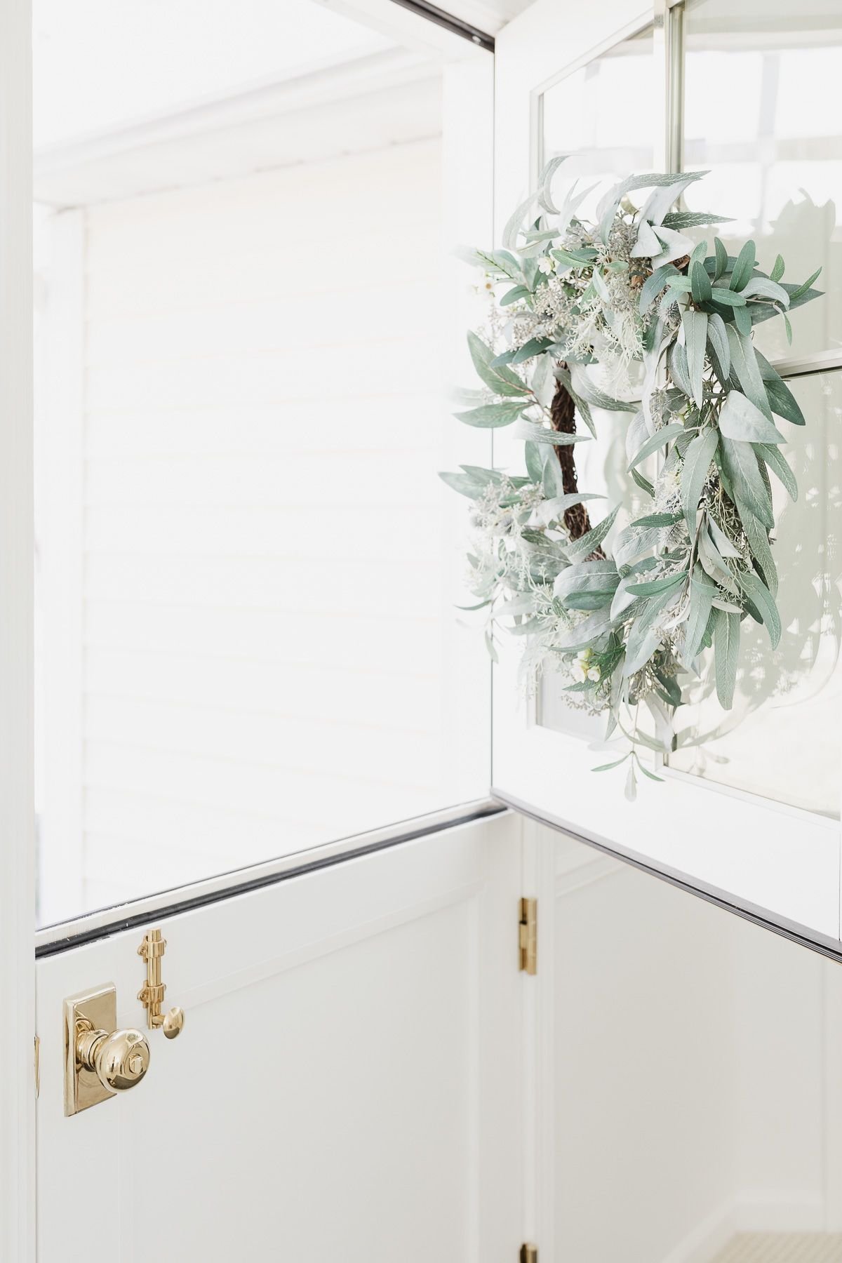 A year-round front door garland with gray-green color on the white door.