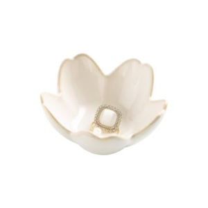 A gold ring with a square white stone rests inside a white, flower-shaped ceramic dish—an elegant touch for nightstand decorating.